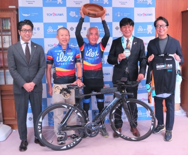 優勝杯を頭上に掲げる中田さんと、谷監督(左隣)。竹本市長(右隣)は優勝メダルをかけてもらった。手前は競技バイク=豊川市役所で
