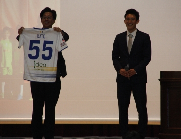 講演した加藤さん㊨から寄贈されたユニホームを披露する鈴木校長=蒲郡市蒲郡中学校で