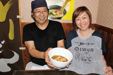 試食用ハーフサイズの豊橋カレーうどんを披露する清水さん㊧と、特製エプロンをPRする協会の西村なぎささん