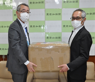 マスクの入った箱を手渡す伊藤統括部長㊧=東愛知新聞社で