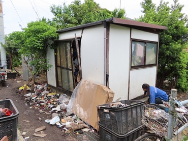 壊れた小屋の前でごみを集める廃棄物収集運搬業者スタッフ
