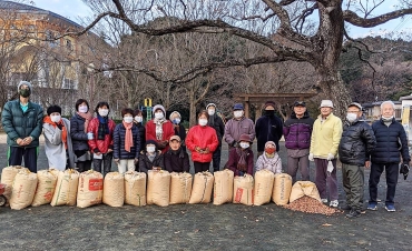 伊藤徹さんを囲む早朝ラジオ体操の会メンバー。手前は集めたドングリの袋=緑ヶ丘公園で