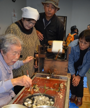 玉繭から糸を取る白井さん㊧、成岡さん(隣り)=豊橋市中部地区市民館で