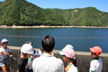ダム湖の上を飛ぶドローンの映像に見入る児童たち=新城市川合の宇連ダムで