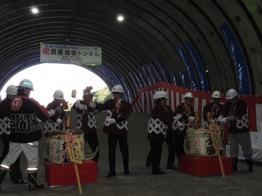 豊川側から差し込む光を浴び、鏡開きで貫通を祝う関係者ら=国坂トンネルで