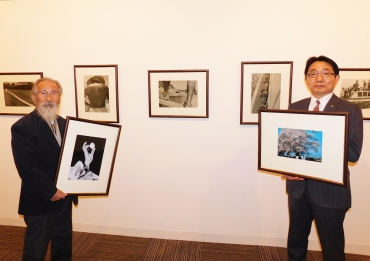 自身の作品の前で東松氏の複製写真を手にする越知氏㊧と、加藤基吉・同ギャラリー所長=名豊ギャラリーで