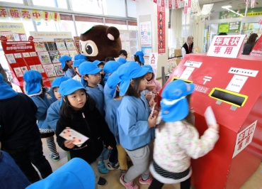 すわポン(後方)が見守る中、年賀状を投函した園児ら=豊川郵便局で