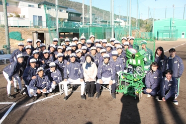 小川投手寄贈のマシンを囲む部員たちと弘子さん=成章高グラウンドで