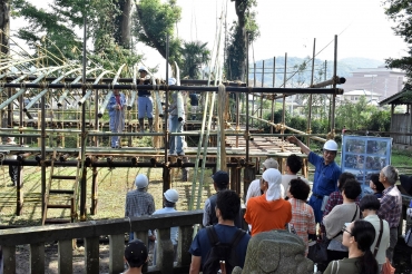 竹を組んで屋根を作る小屋掛け作業を見学する人たち=杉森八幡社で