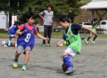 ドリブル練習で競り合う児童たち(後方は大島コーチ)=東栄町総合グラウンドで