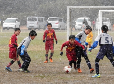 雪が激しく舞う中、安城北部FC(灰色)とボールを追うアルテス東田FC(赤色)=かもめグラウンドで