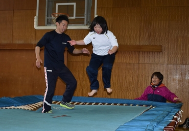 伊藤さん㊧とトランポリンで跳ぶ女子生徒=豊川特別支援学校で