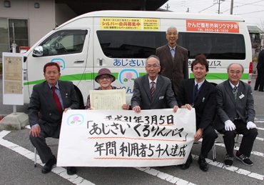 バスの前で記念品を手にする鈴木さん(左から2人目)=蒲郡市形原公民館で
