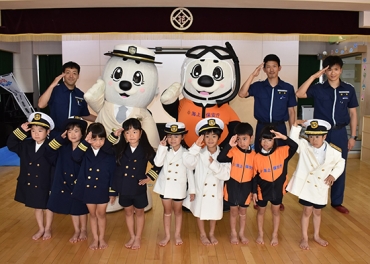 髙橋さん㊨ら署員と海上保安庁の制服で敬礼する子どもたち=花井幼稚園で