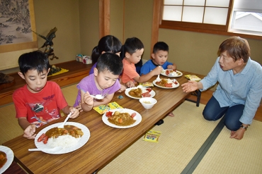 櫻井所長㊨と談笑しながらカレーライスを食べる子どもたち=豊地区市民館で