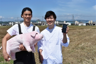 自身の養豚場を背にプロジェクトをPRする山本さん㊧と夏目さん=西尾市内で