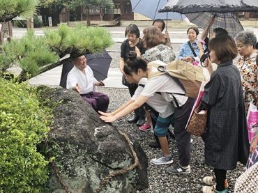 さざれ石に手を触れる女性参加者たち=砥鹿神社で(豊川市観光協会提供)