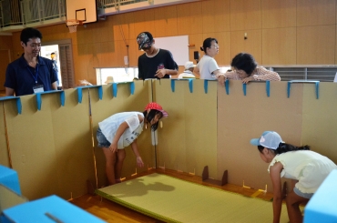 避難所の間仕切りを組み立てる参加者=小沢小学校で