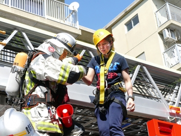 外国人女性㊨がはしご車から降りるのをサポートする消防隊員=県営岩田住宅で