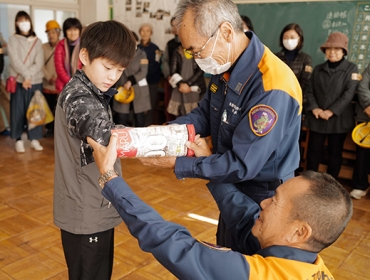 小学生の骨折した腕にラップを巻き、さらに雑誌をラップで固定する消防本部職員=花田小学校で
