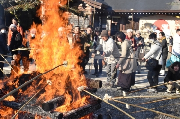 勢いよく燃える炎に竹棒を伸ばし、餅を焼く参拝者ら=砥鹿神社で