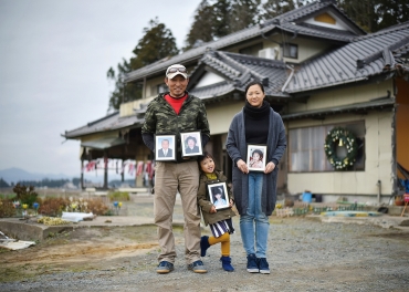 津波で壊れた自宅前で亡くなった4人の遺影を持つ上野さん一家=福島県南相馬市で(笠井さん提供)