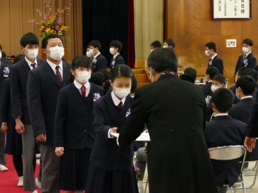 マスクを着用し、簡略化した所作で卒業証書を受け取る卒業生ら=豊城中学校で