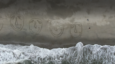 海岸に描かれた大小の顔、右の人影は山本さんら(ドローンの映像から)