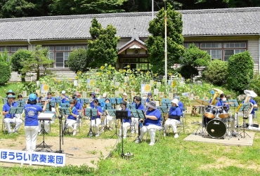 展示された花と演奏する吹奏楽団メンバー=新城市門谷の旧門谷小学校で(提供)