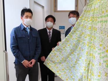 贈られたカーテンと花島さん、深谷社長、瀧川公園長(左から)