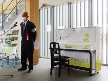 菜の花模様でラッピングされた「菜の花ピアノ」を横にあいさつする山内会長=三河田原駅で