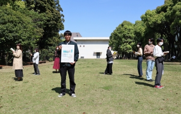 図書館をイメージしたパフォーマンスを披露する学生と上田准教授(中央)=愛大のそよかぜ広場で